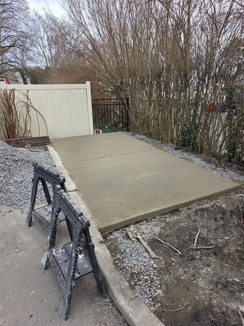 Freshly poured concrete pad along a fence line