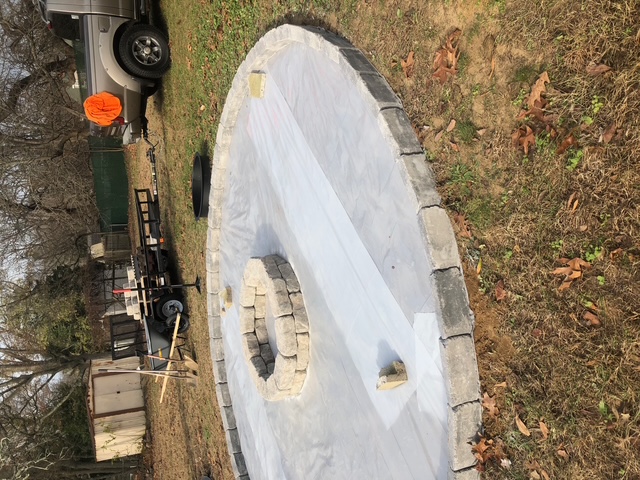 Round paver fire pit patio under construction with stone border and inner ring