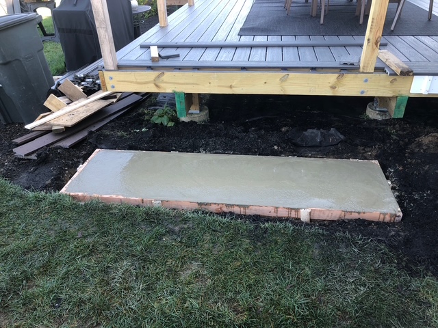 Freshly poured and finished concrete pad at the base of deck steps